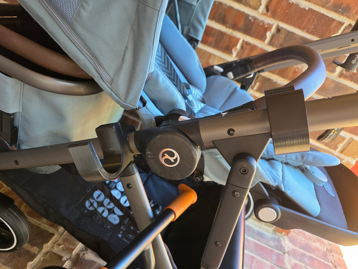 Close-up of two black PETG holders clipped to the upper side frame tube of a light blue CYBEX eGazelle S, cradles empty and facing up, spaced apart along the tube.