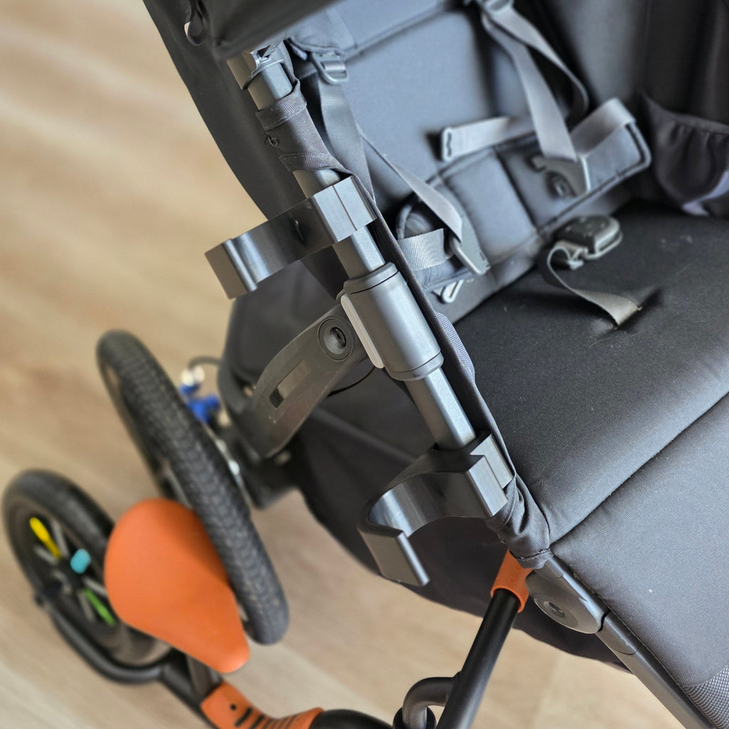 Close-up of two black PETG holders clipped to the side frame tube of an UPPAbaby Ridge, cradles empty and facing up, spaced apart along the tube.