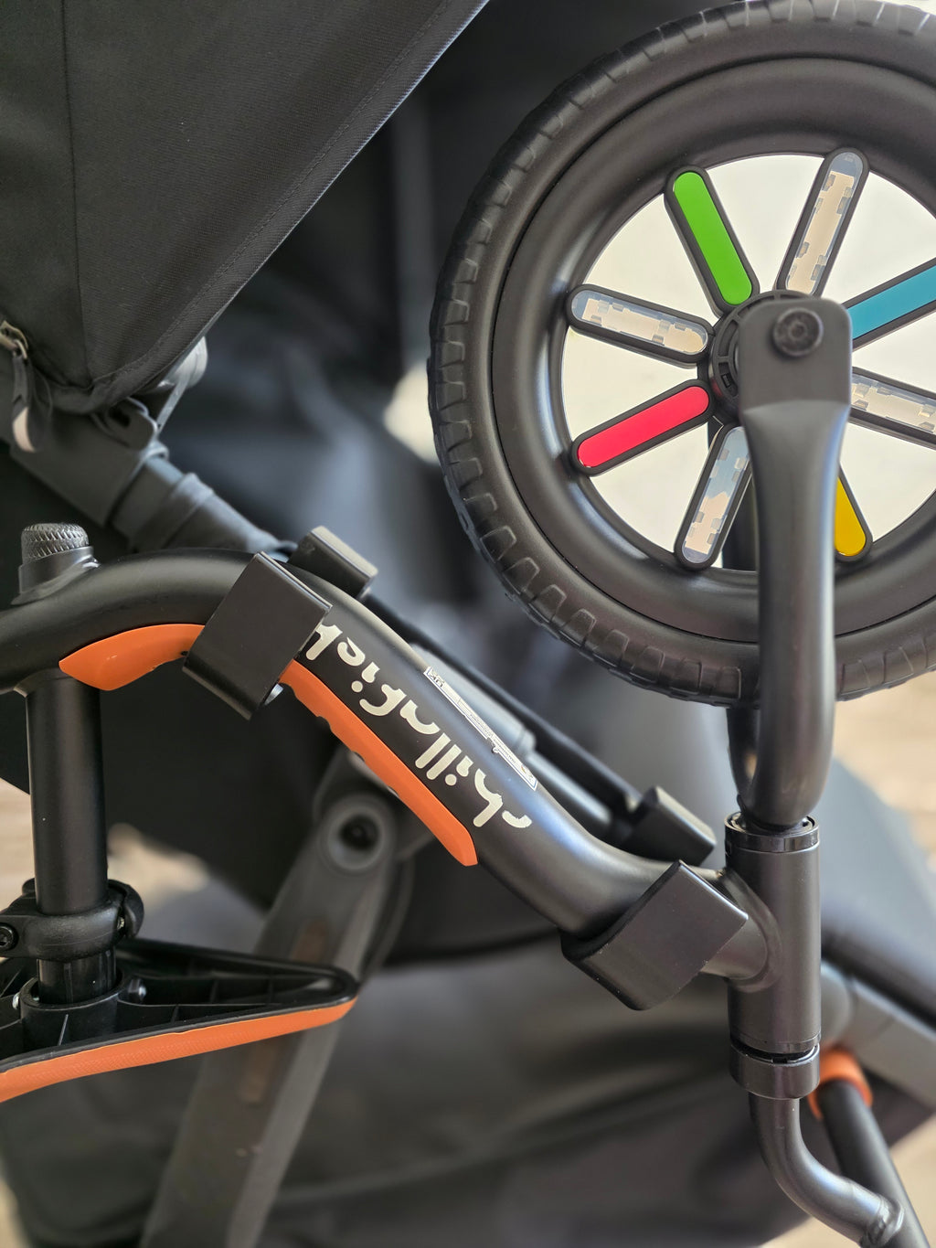 The balance bike's frame resting in the two black holders on the UPPAbaby Ridge side tube, held by its own weight with no strap.