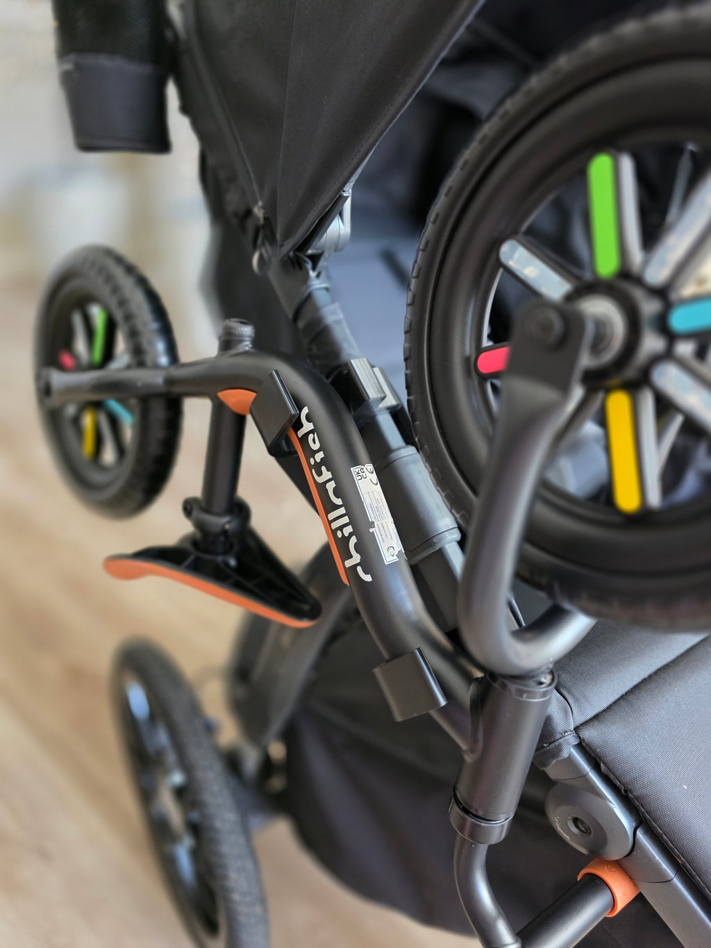 The balance bike carried on the side of the UPPAbaby Ridge, hanging clear of the stroller's rear wheel.