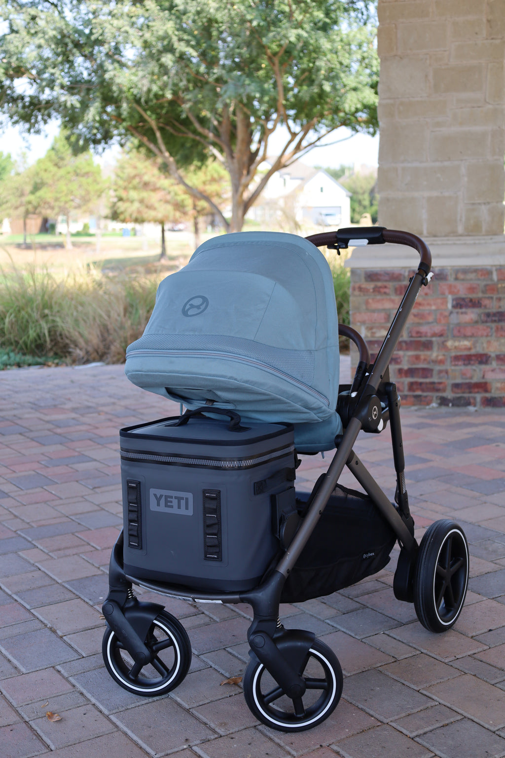 Side view of a CYBEX Gazelle S carrying a charcoal YETI Hopper Flip 12 on the cooler mount under the seat, with the storage basket below left open for bags and jackets
