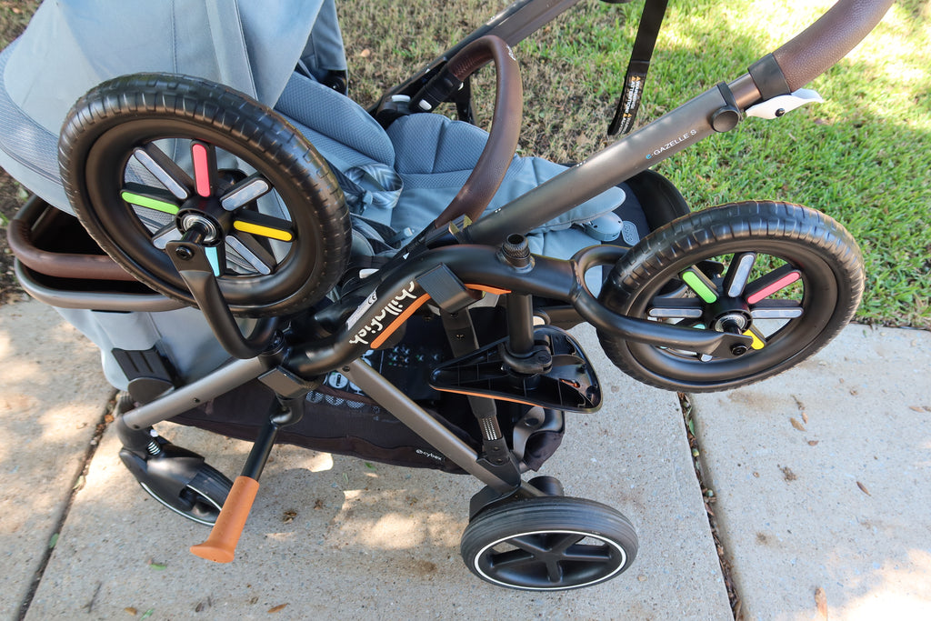 Front three-quarter view of the loaded CYBEX eGazelle S, the e-GAZELLE S badge visible on the frame tube, the balance bike's wheels sitting clear of the stroller's wheels.