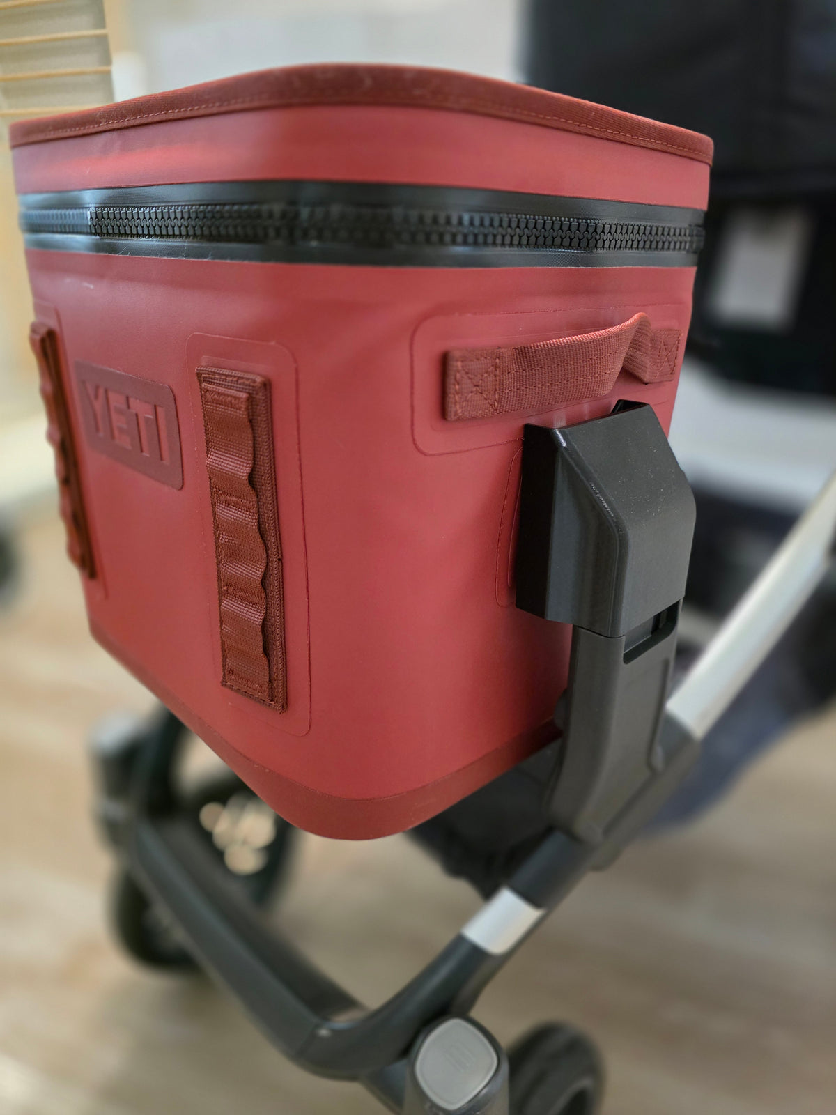 Close-up of the black Stroller House cooler mount holding a YETI Hopper Flip 12 by its side handle on an UPPAbaby Vista lower adapter