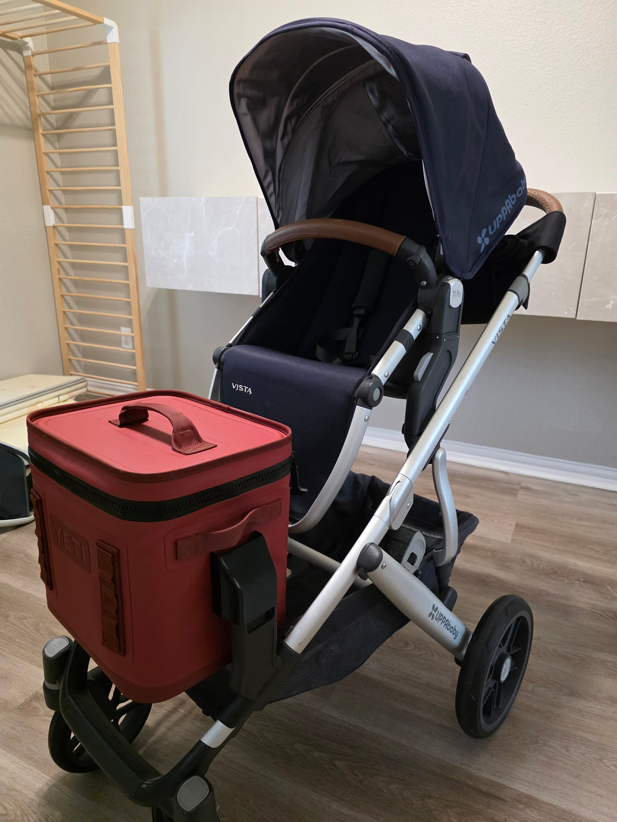Red YETI Hopper Flip 12 carried low on the side of an UPPAbaby Vista on the Stroller House cooler mount for the 2024 and newer lower adapters, with the seat and canopy above it