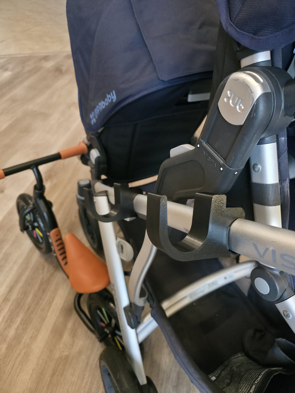 A single black holder clipped to the UPPAbaby Vista frame tube, showing the open cradle that a balance bike's top tube drops into.