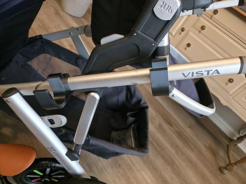 Close-up of the two black PETG holders clipped to the UPPAbaby Vista's upper side frame tube, cradles empty and facing up, spaced apart along the tube.